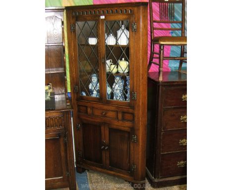 A reproduction Oak Priory style floor standing Corner Cabinet with moulded top over carved frieze, in turn over a pair of opp