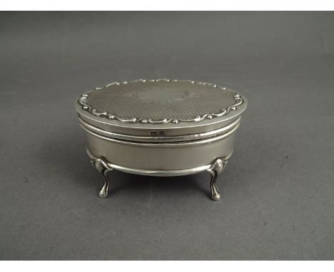 A silver oval trinket box raised on four cabriole feet, engine turned detail, vacant cartouche, pink velvet lined interior, B