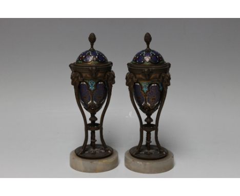 A PAIR OF CHAMPLEVE ENAMEL GARNITURE / CANDLE HOLDERS, urn shaped holder with enamel decoration, set within a tripod stand wi