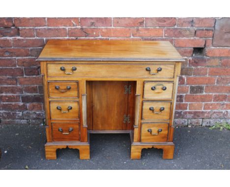 A 19TH CENTURY MAHOGANY KNEEHOLE DESK, having an arrangement of seven drawers around an inset central cupboard, raised on bra