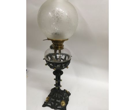A Victorian oil lamp with gothic influences with glass shade and chimney.
