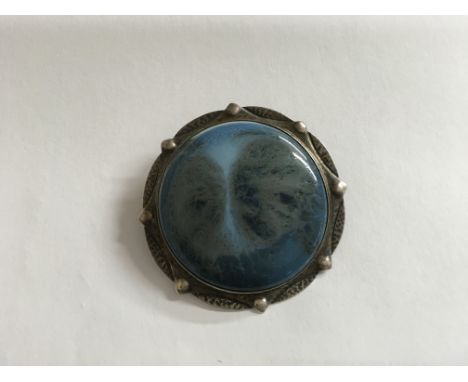 An Arts and Crafts, Liberty style brooch; white metal mounted with large blue ceramic roundel.Approx 5x5cm
