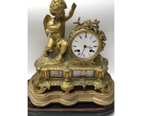 A gilt ormolu French mantle clock the enamel dial with Roman numerals flanked by a cherub inset with Serves style panels.