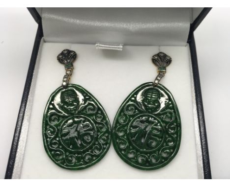 A pair of oval shaped patterned jade drop earrings set with emeralds and diamonds, boxed