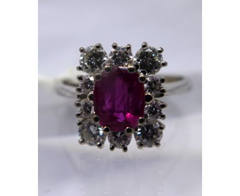 An 18ct white gold, natural ruby and diamond cluster ring, the central oval faceted natural ruby in 6-claw mount and framed b