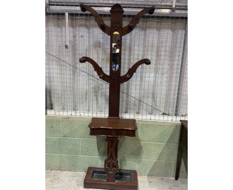 An Art Nouveau style hall stand with eight coat hooks surrounding a portrait mirror and storage compartment drip tray to base