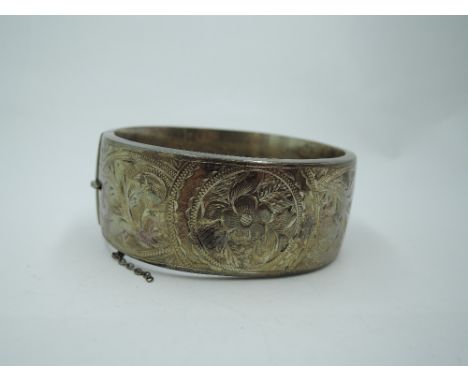 A silver hinged bangle of broad form having engraved scroll and floral decoration, approx 39g