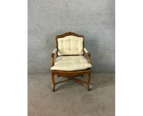 A late 19th century French carved beech framed open arm upholstered button back and cane chair raised on carved supports term