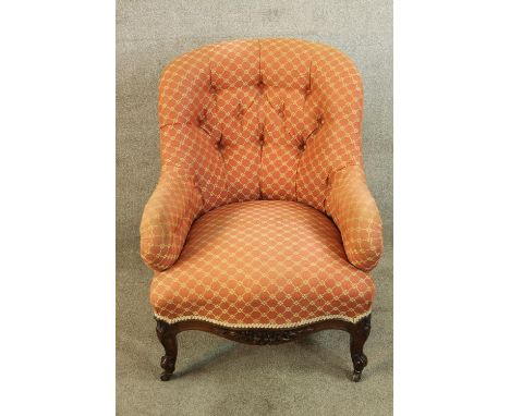 A 19th century carved mahogany framed button back low nursing chair raised on carved cabriole supports terminating in casters