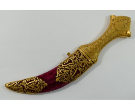 An Indian jambiya dagger, with gilt metal handle and curved steel blade, the red fabric covered scabbard with pierced and cas