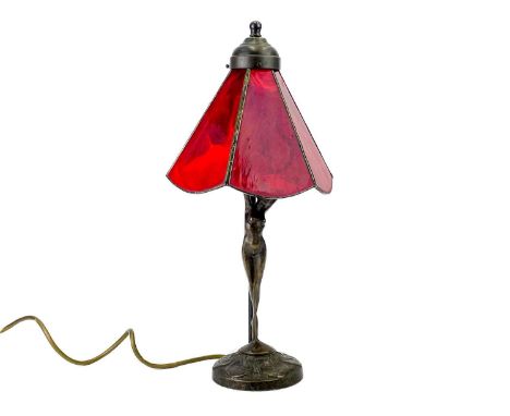 A bronzed metal figural table lamp base after Moreau, modelled with a female nude. With Tiffany style red glass shade. Height