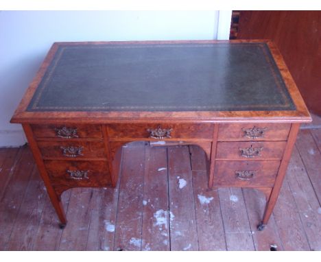 An Edwardian burr walnut and oak writing desk.  The top with moulded edge inset with gilt tooled leather above an arrangement