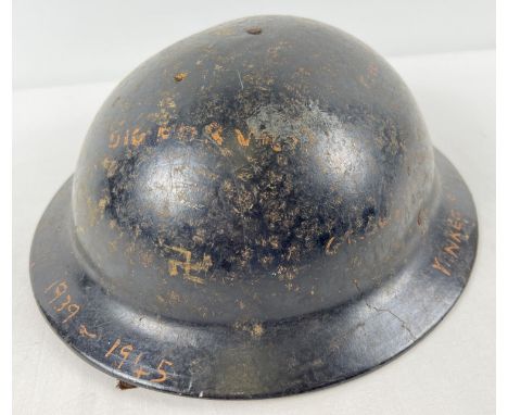 A British Bakelite MkII style Home Front helmet with cruciform pad. Black with numerous wartime painted slogans on e.g Put th