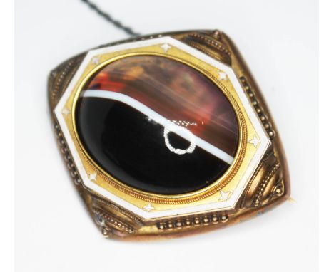 A Victorian Revivalist yellow metal and enamel brooch set with a central foiled back banded agate cabochon, length 49mm, gros