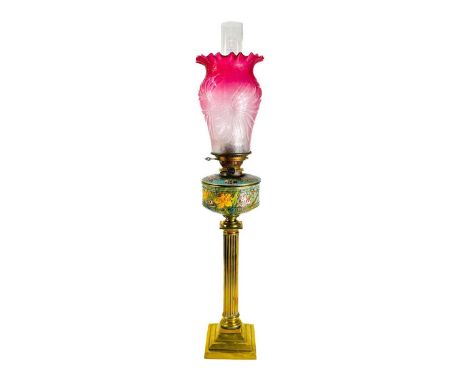 A Victorian cranberry shade brass oil lamp. With ceramic painted reservoir, height 88cm.There is a small crack to the bottom 