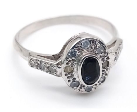 An 18 K white gold ring with a central dark blue sapphire and diamonds on the halo and shoulders. Ring size: O, weight: 2.8 g