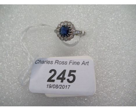 A diamond and sapphire cluster ring, the cornflower blue stone claw mounted to a plain white metal shank.