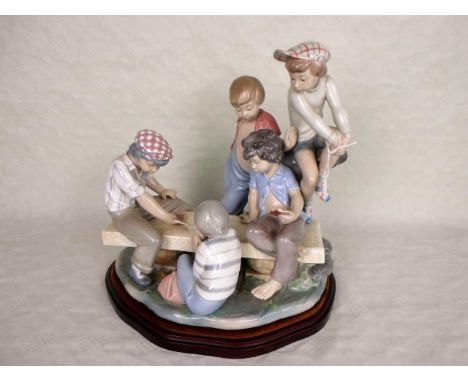 A large Nao figure group, children playing cards, mounted to bespoke wooden stand, 34cm tall.