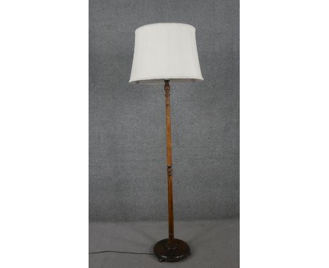 A circa 1920s walnut standard lamp, with a white shade, the stem turned in some places, on a circular base with three ball fe