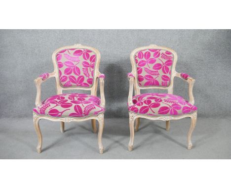 A pair of 20th century French Louis XV style fauteuil armchairs, with limed frames, upholstered in foliate pink and light gre