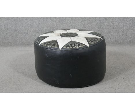 A Middle Eastern pouffe, of circular form, black with an ivory coloured flowerhead top, decorated with camels, trees, and mai