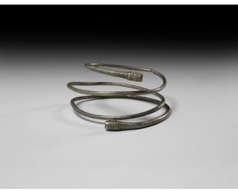 10th century AD. A coiled silver arm-ring, round in section with clubbed terminals, bands of incised scrolls and loops, lion(