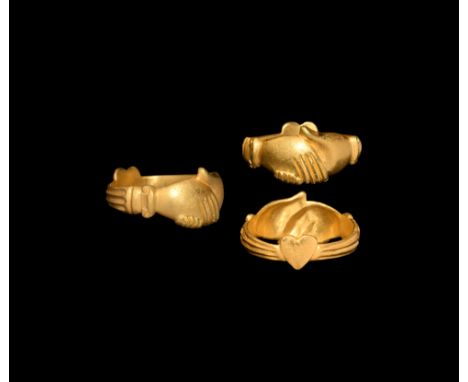 17th-18th century AD. A gold finger ring formed as two clasped hands with scrolled cuffs and ribbed hoop, heart-shaped plaque