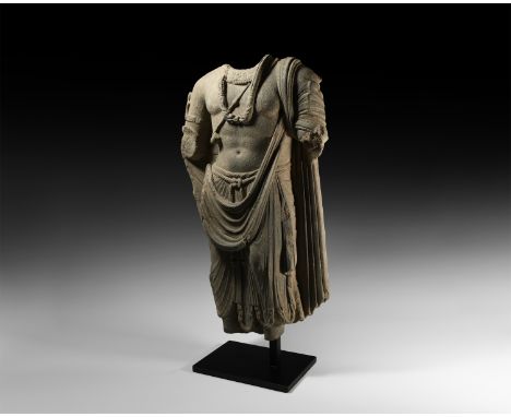 1st-3rd century AD. A carved schist statue of Bodhisattva Maitreya standing, wearing a loose mantle and dhoti, with floral co