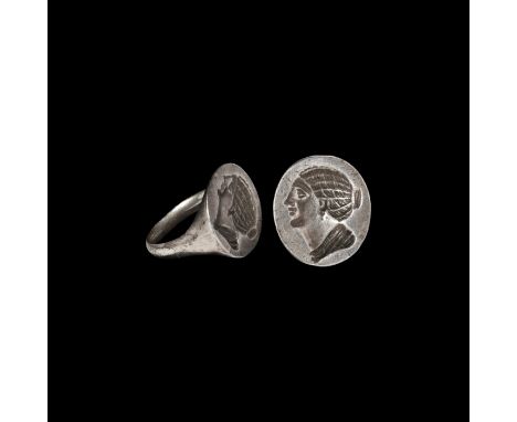 3rd-2nd century BC. A silver finger ring with flared discoid plaque, intaglio profile female bust with braided hair drawn bac