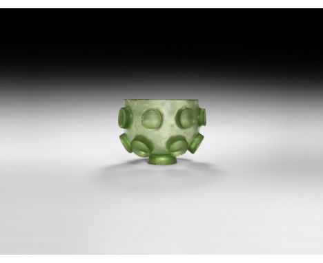 6th-7th century AD. A green glass small bowl or cup cut with concave relief bosses, eight to the upper row and six below, and