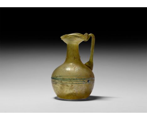 1st-2nd century AD. A small green glass collared globular jug with short neck, angular ribbon handle with two narrow prominen