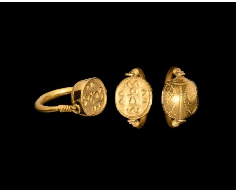 6th-4th century BC. A gold finger ring with round-section hoop and spiral-wound ends, the bezel a hollow-formed gold scaraboi