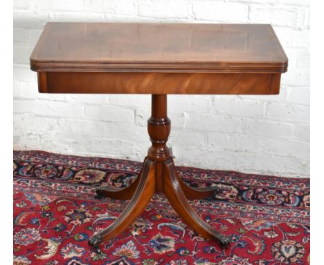 A reproduction mahogany fold-over card table, the swivel fold-over top enclosing baize material, raised on baluster column te