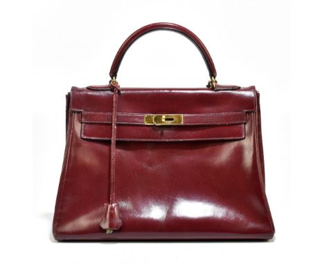 HERMES; a vintage 1962 burgundy leather Kelly 32 handbag, with a D-shaped handle and detachable shoulder strap, and gold tone