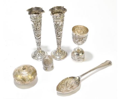 A pair of Indian white metal vases decorated throughout with figures, animals and buildings in a landscape, on circular feet,