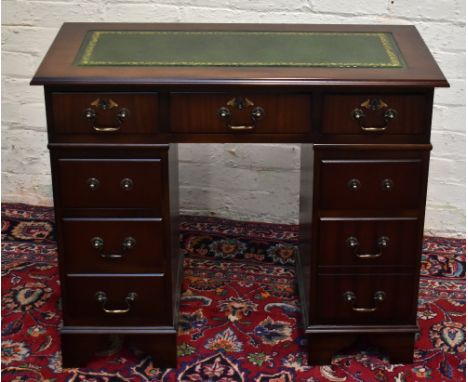 A reproduction mahogany desk with green leather inset top above an arrangement of eight drawers, raised on bracket feet, widt