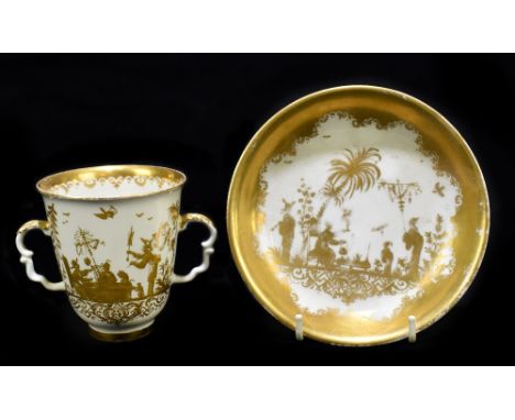 An early 19th century gilt decorated cream ground twin handled cup and saucer decorated with Chinoiserie figures, unmarked, d