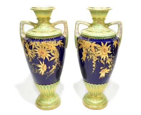 ROYAL WORCESTER; a pair of twin handled pedestal vases with moulded floral and gilt heightened detail on a cobalt and green c
