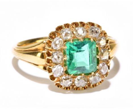 A yellow metal diamond ring with central emerald coloured stone within a border of twelve old cut diamonds, in high claw sett