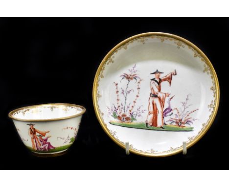 An 18th century Continental tea bowl and saucer decorated with Chinoiserie figures, the bowl with puce floral spray to the ce