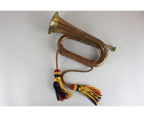 A copper and brass bugle with red, blue and gold braid and tassels
