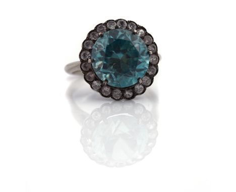 A BLUE ZIRCON AND COLOURLESS GEM SET CLUSTER RINGClaw set with the circular cut blue zircon in a surround of colourless gems,