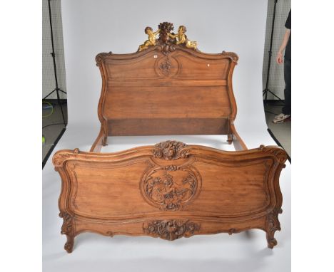 A 19TH CENTURY FRENCH CARVED WALNUT DOUBLE BEDWith opposing gilt cherub crest, united by shaped side supports; 161cm wide; 14