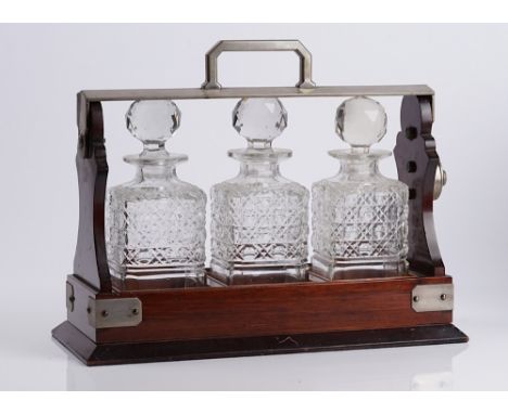AN EDWARDIAN MAHOGANY THREE BOTTLE TANTALUSWith nickel plated mounts, cut glass bottle and stopper, 38cm wide; 16cm deep; 30.