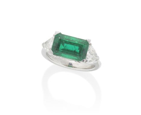 MANUFACTURE IN ART: EMERALD AND DIAMOND RINGThe step-cut emerald, weighing 4.30 carats, set horizontally between triangular-c