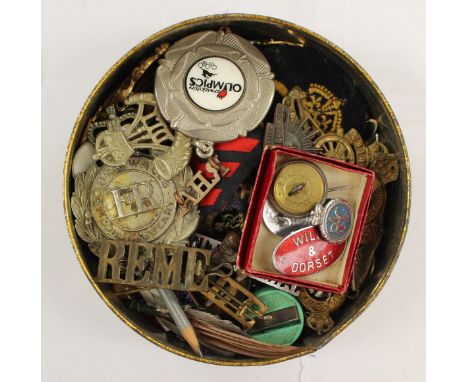 A collection of military cap badges and enamel lapel badges in a vintage CWS Biscuit tin to include: RA, DLI, RAOC, Royal Sig