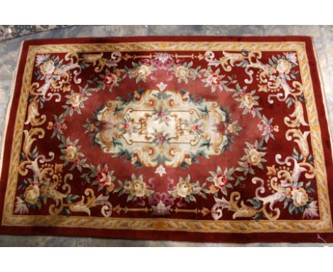 A Chinese style woollen rug, red ground with gold border, pink and cream central panel embellished with floral and scroll des