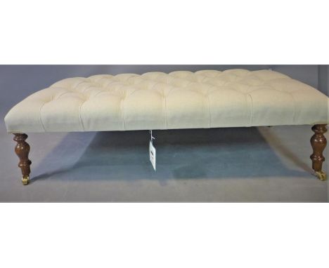 A Howard style hearth stool, with deep button linen upholstery, on turned legs and castors, H.35 W.122 D.61cm 