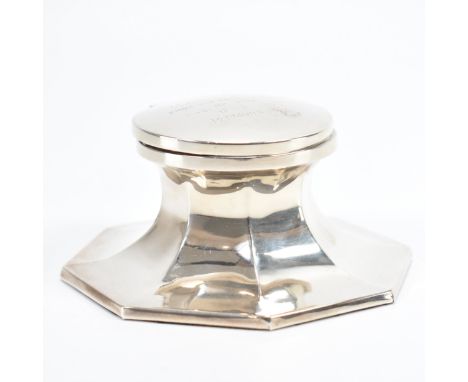 An Art Deco hallmarked silver lidded inkwell. The inkwell of circular form on a faceted octagonal base with fitted glass line