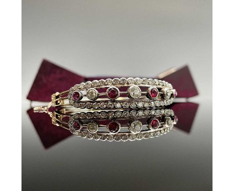 An exquisite Victorian gold diamond and ruby bangle, the central oval panel set with three round cut diamonds and four rubies